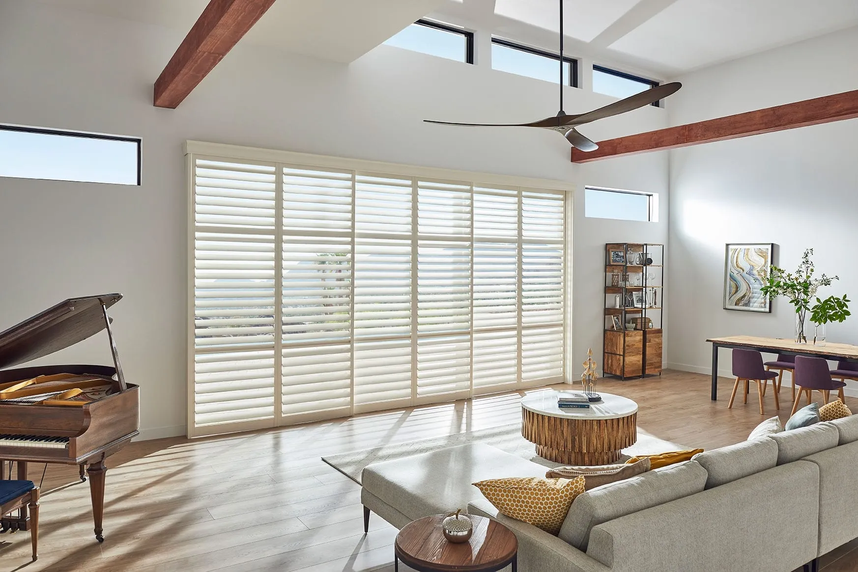 Alta shutters across a tall wall of windows in a living room with a piano