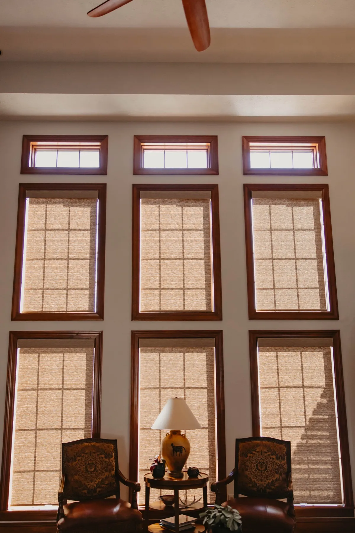Tall wood-trimmed windows with screen shades lowered behind two armchairs