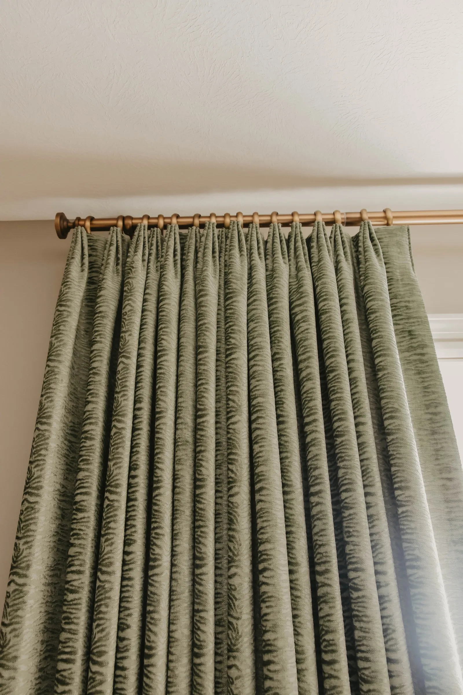 Custom green pinch-pleat drapery on a brass rod