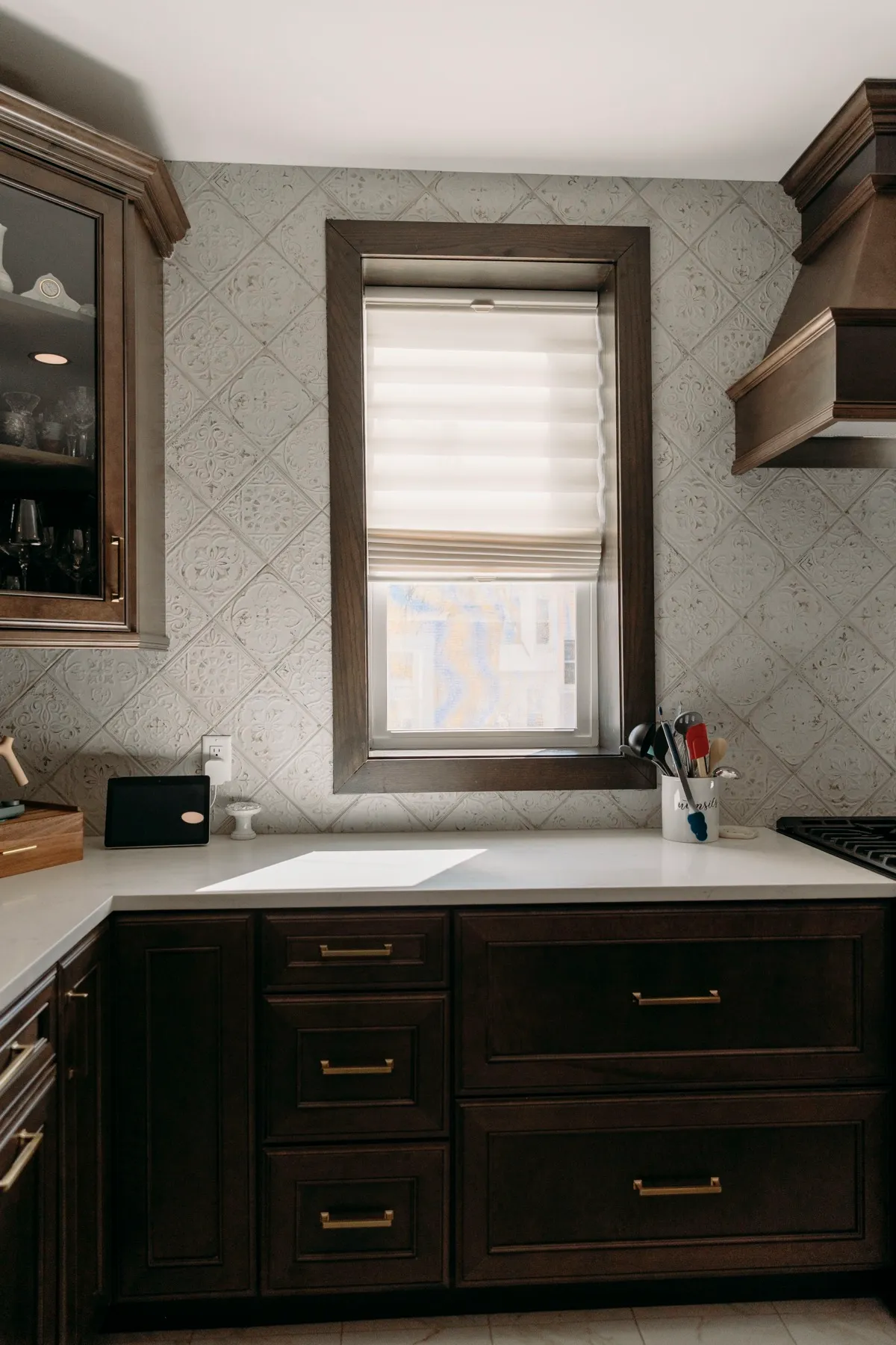 Kitchen window with a roman shade above dark cabinets