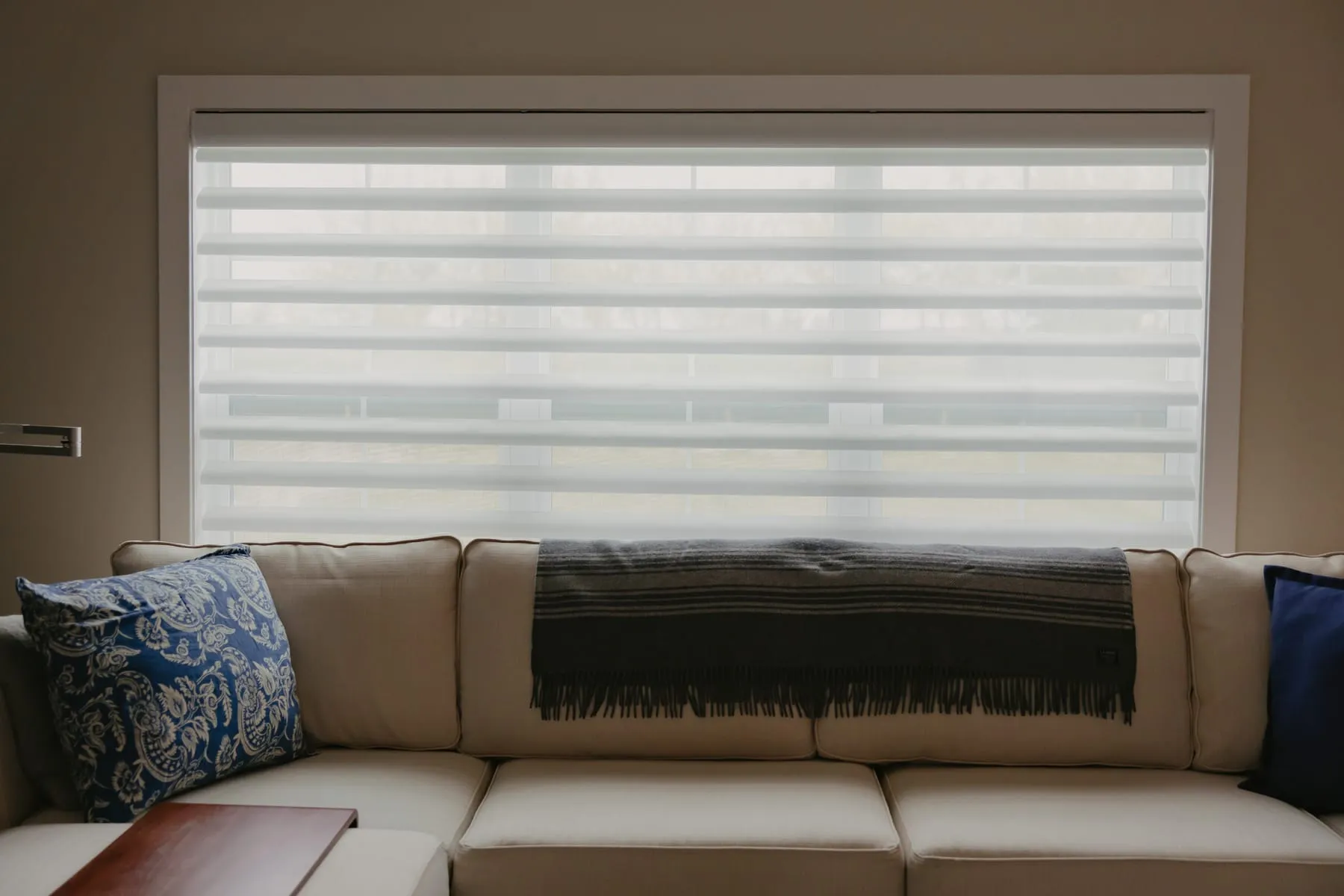 Sheer shades on a wide window behind a sectional sofa
