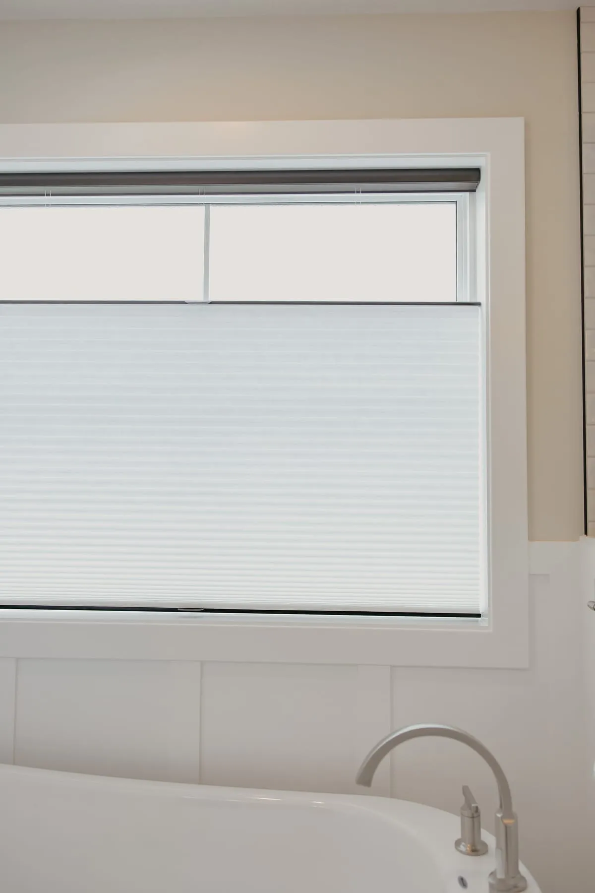 Shade lowered from the top on a bathroom window above the tub