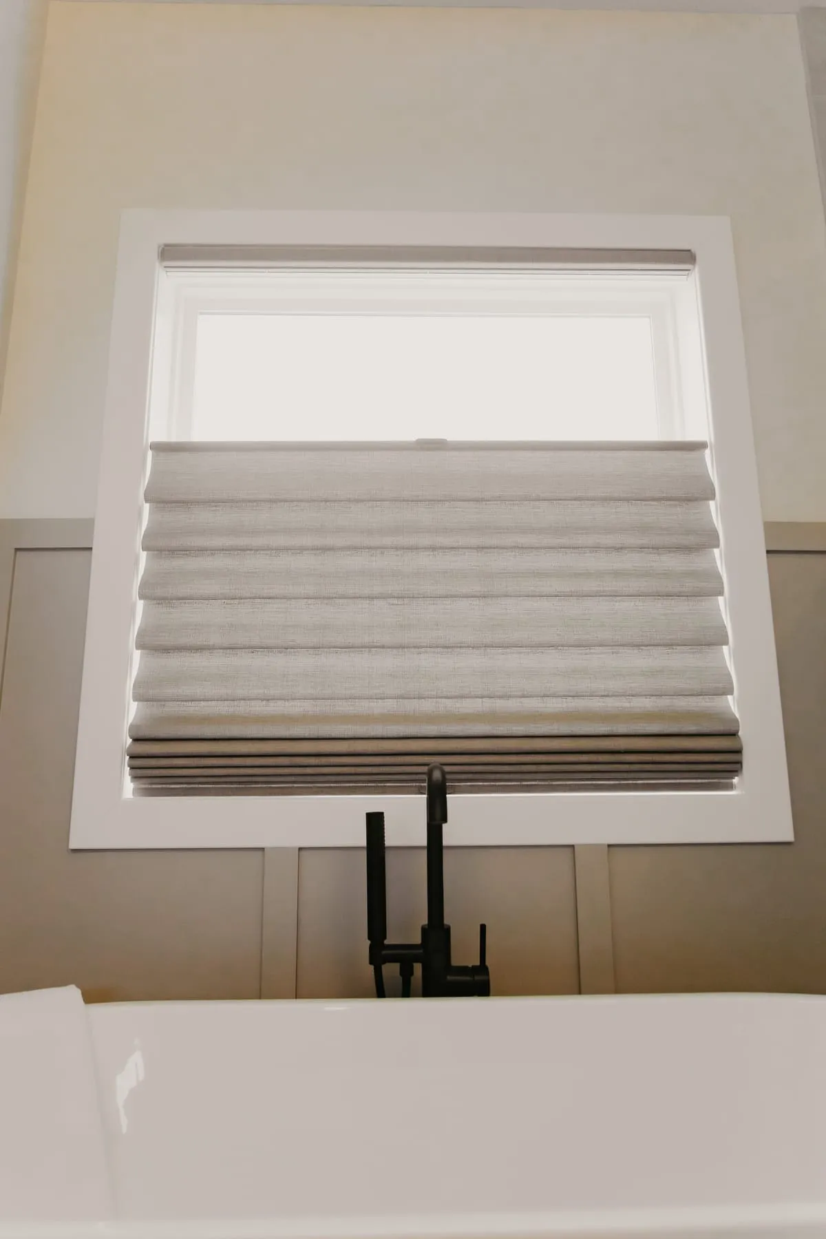 Pleated shade on a bathroom window above a freestanding tub