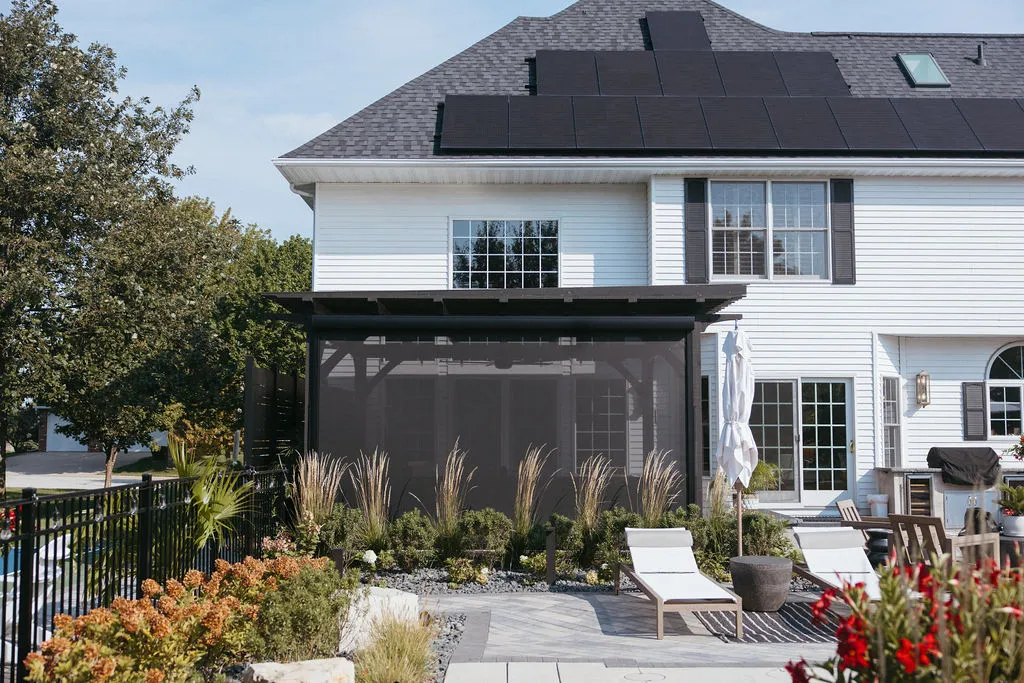 Dark pergola with MagnaTrack screens lowered beside a pool and landscaped patio
