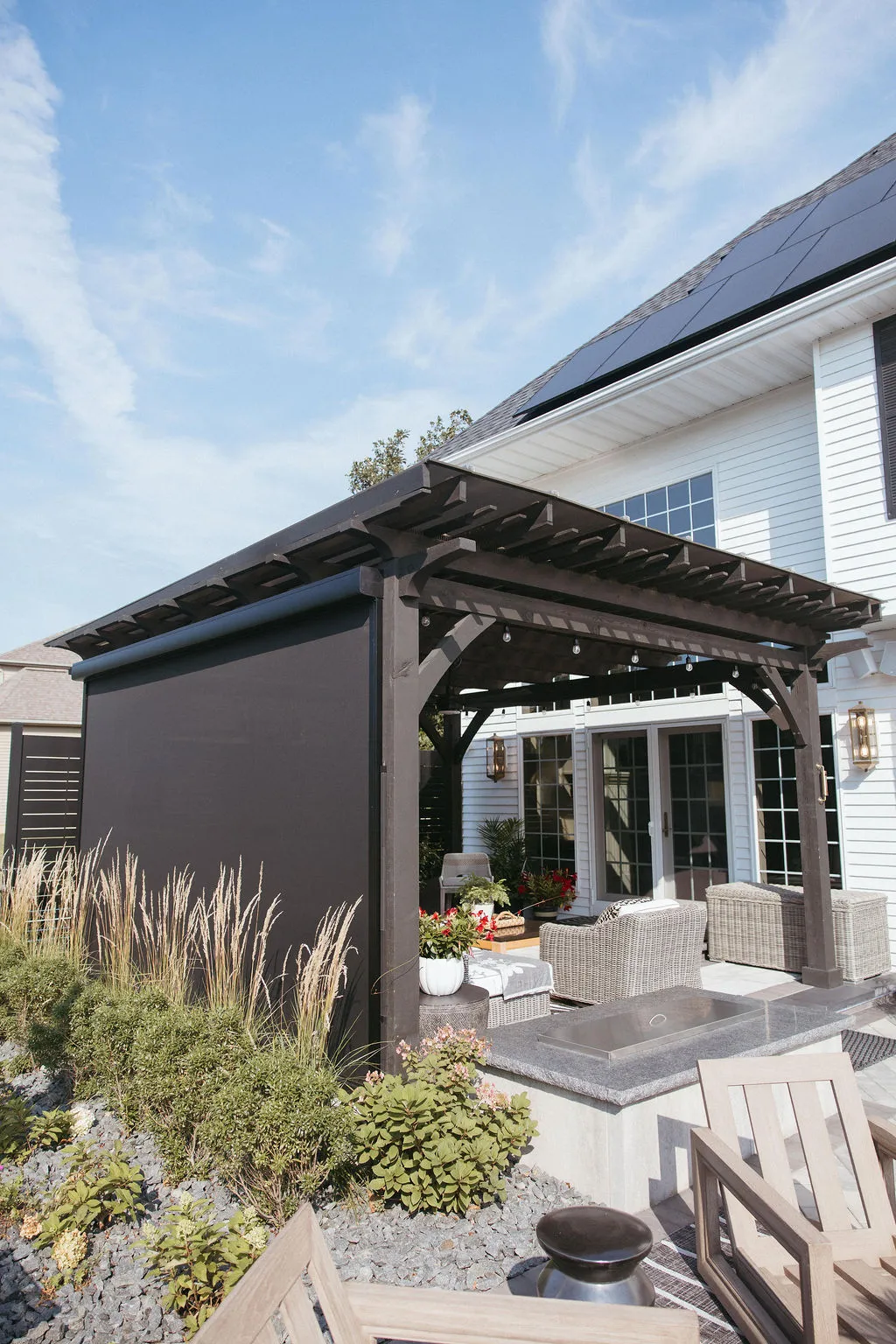 Dark pergola with MagnaTrack screens lowered on a landscaped patio