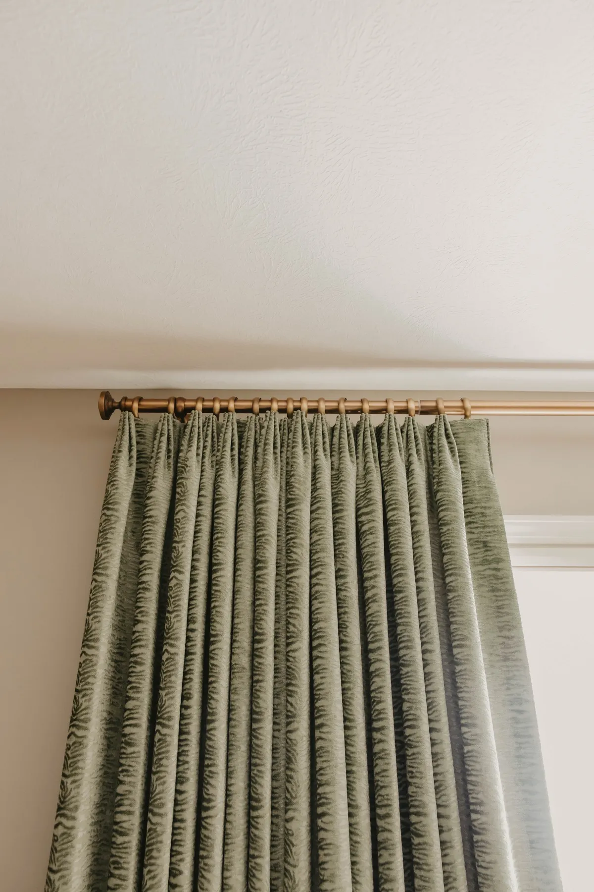 Green patterned pleated draperies hung from a brass rod