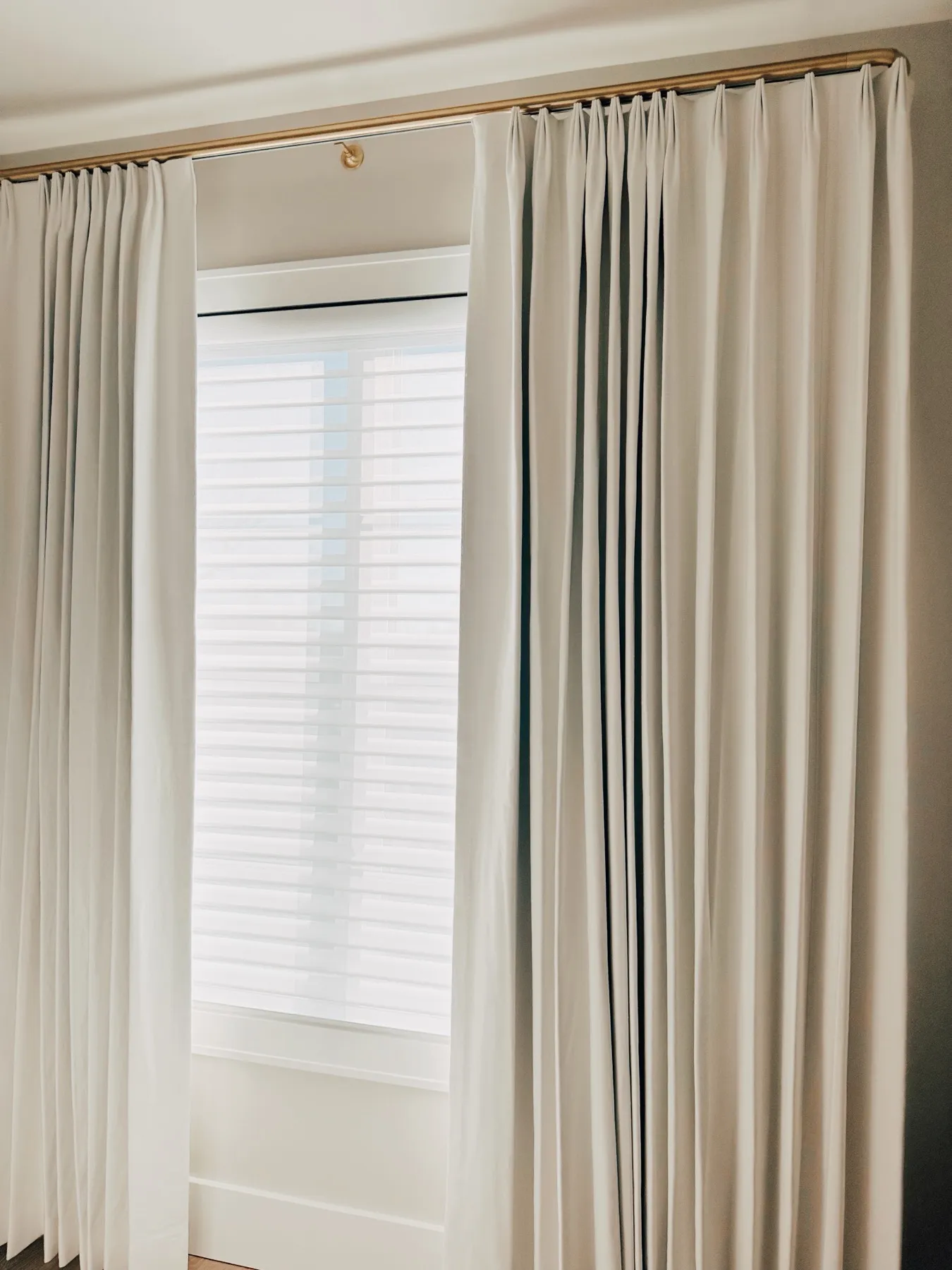Ivory pleated draperies framing a window with shades