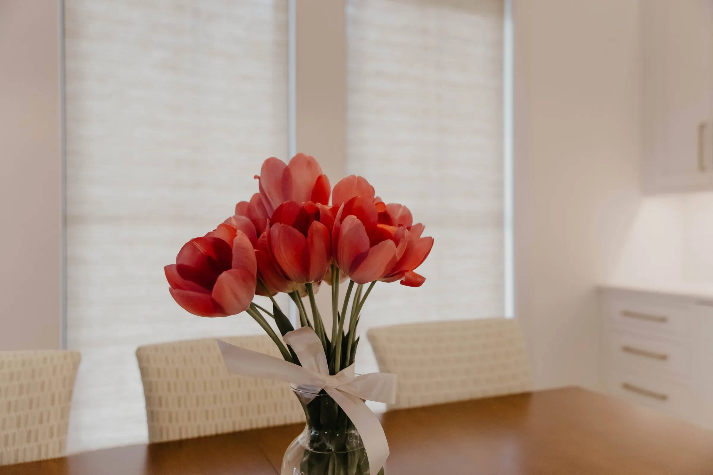 Shades filtering soft daylight behind a vase of tulips